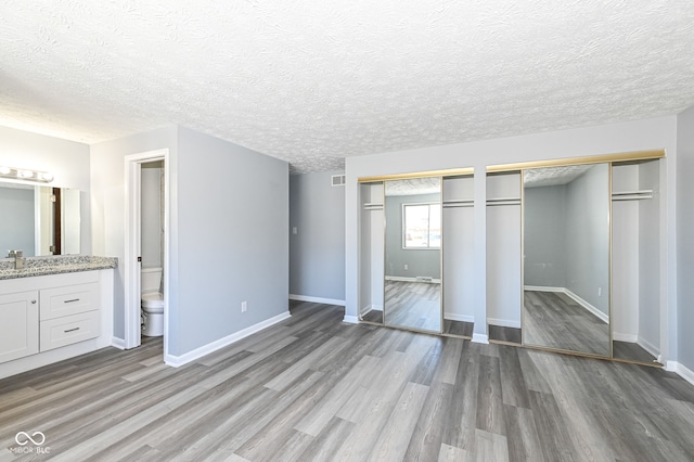 unfurnished bedroom featuring multiple closets, ensuite bathroom, sink, and light hardwood / wood-style flooring