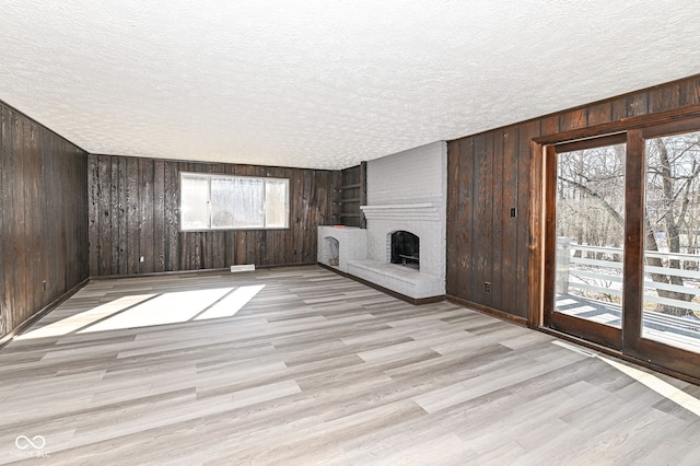 unfurnished living room with light wood-type flooring, a fireplace, a textured ceiling, and wood walls