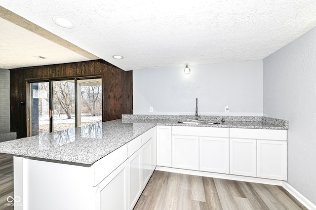 kitchen featuring sink, light hardwood / wood-style flooring, white cabinets, and kitchen peninsula