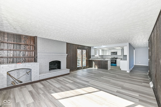 unfurnished living room with a brick fireplace, a textured ceiling, and light wood-type flooring