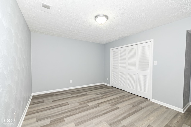 unfurnished bedroom featuring a closet, a textured ceiling, and light hardwood / wood-style flooring