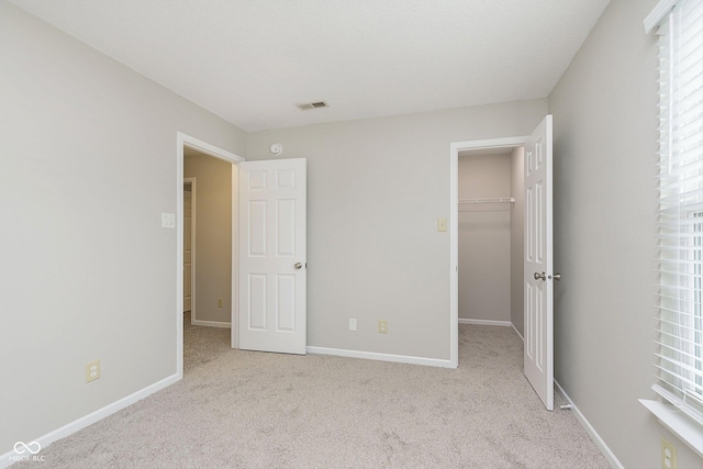 unfurnished bedroom featuring a walk in closet, light carpet, and a closet