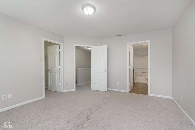 unfurnished bedroom featuring light carpet, connected bathroom, and a textured ceiling