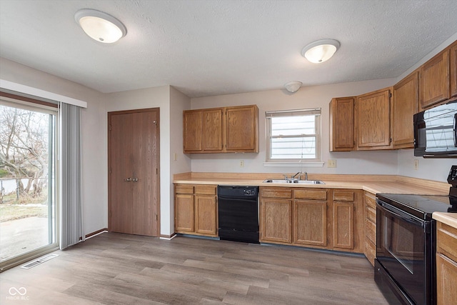 kitchen featuring sink, a textured ceiling, light hardwood / wood-style floors, and black appliances