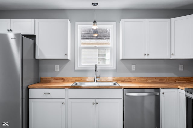 kitchen with sink, butcher block countertops, white cabinetry, hanging light fixtures, and appliances with stainless steel finishes