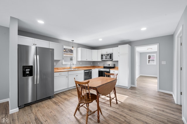 kitchen featuring sink, white cabinetry, decorative light fixtures, light wood-type flooring, and stainless steel appliances