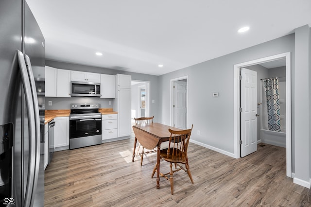 kitchen featuring light wood-type flooring, wooden counters, white cabinets, and appliances with stainless steel finishes