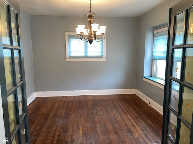 unfurnished room featuring a healthy amount of sunlight, dark hardwood / wood-style flooring, and a notable chandelier