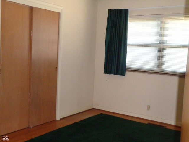 unfurnished bedroom featuring hardwood / wood-style flooring, a closet, and multiple windows