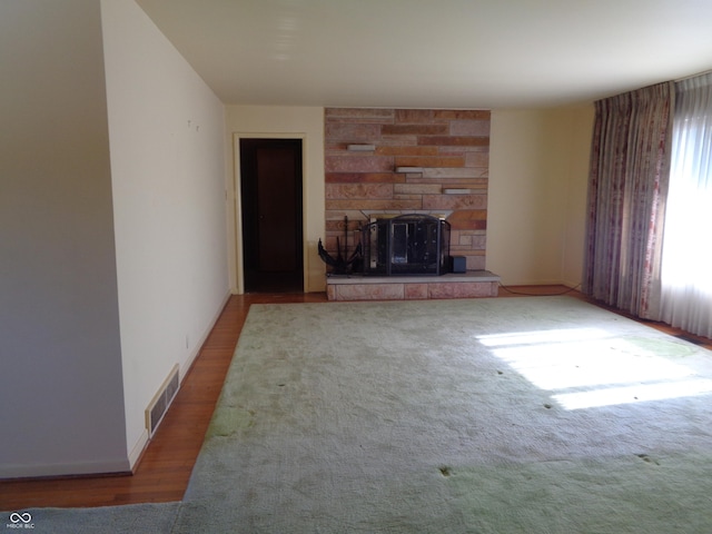 unfurnished living room with wood-type flooring and a stone fireplace