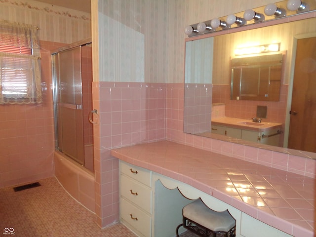 bathroom with vanity, tile patterned flooring, combined bath / shower with glass door, and tile walls