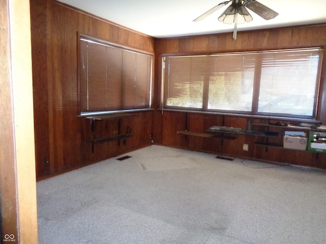 carpeted spare room with ceiling fan and wood walls