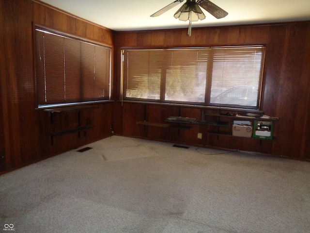 carpeted empty room featuring wooden walls and ceiling fan