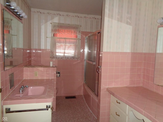 bathroom featuring enclosed tub / shower combo, vanity, tile patterned flooring, and tile walls