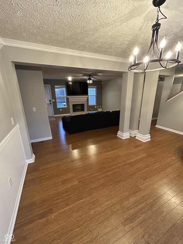 unfurnished living room with ornamental molding, dark wood-type flooring, a textured ceiling, and ceiling fan