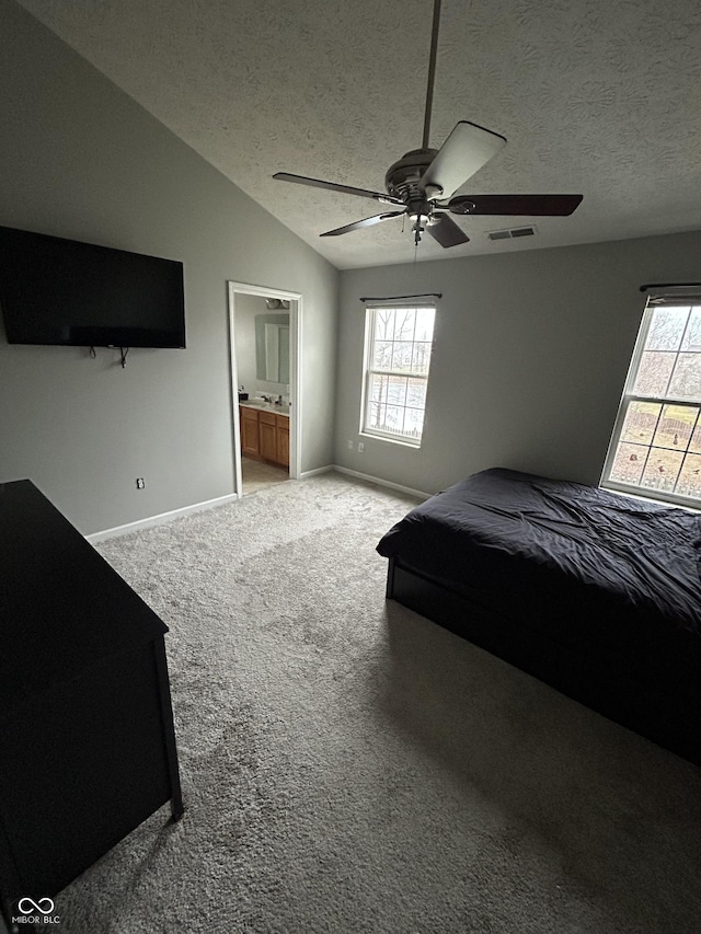 bedroom featuring ensuite bathroom, vaulted ceiling, a textured ceiling, carpet floors, and ceiling fan