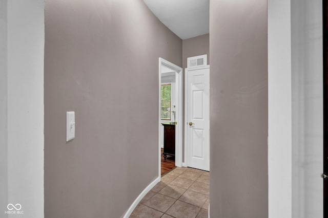 corridor featuring baseboards, visible vents, and light tile patterned floors