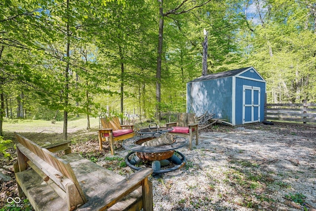 view of yard featuring a fire pit, fence, a shed, an outbuilding, and a wooded view