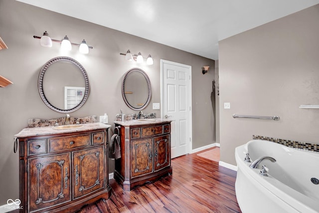 full bath with a garden tub, wood finished floors, two vanities, a sink, and baseboards