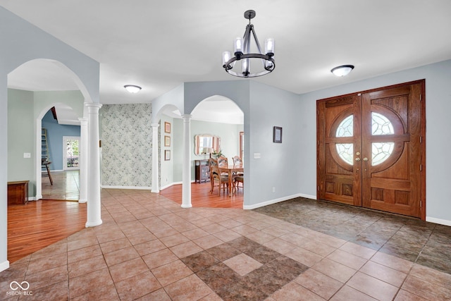 foyer with baseboards, wallpapered walls, arched walkways, and a notable chandelier