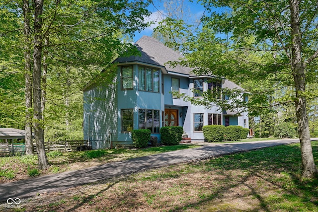 victorian home with roof with shingles, fence, and stucco siding