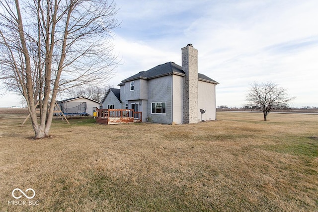 rear view of property featuring a trampoline, a lawn, and a wooden deck