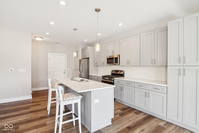 kitchen with sink, a kitchen island with sink, hanging light fixtures, stainless steel appliances, and a kitchen bar