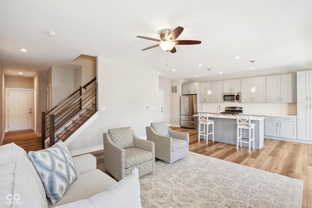 living room featuring sink, ceiling fan, and light wood-type flooring