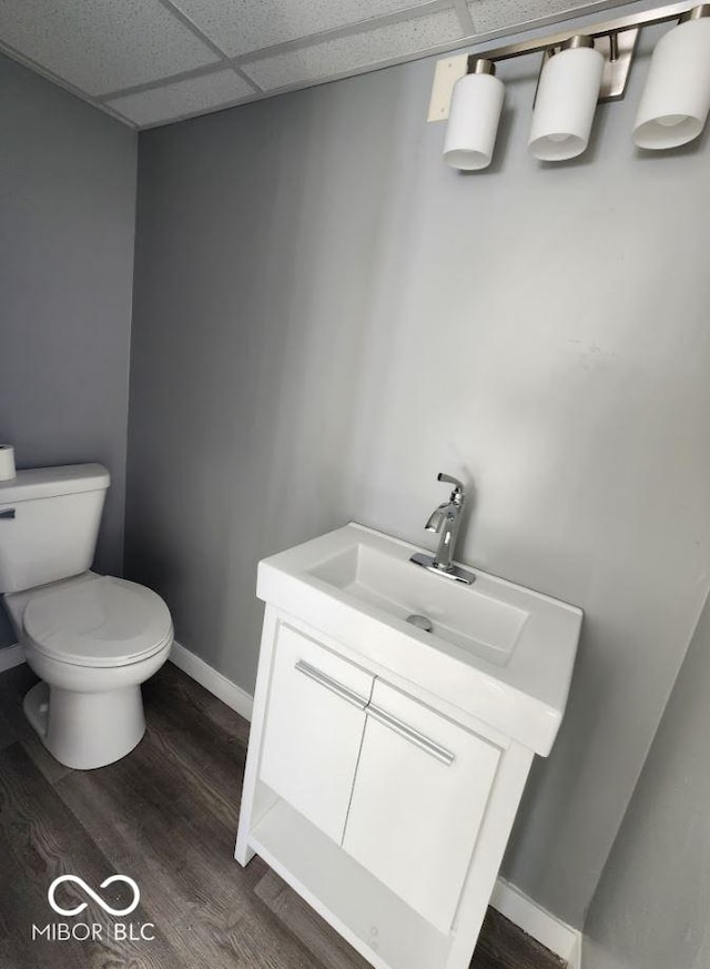 bathroom featuring hardwood / wood-style flooring, vanity, a drop ceiling, and toilet