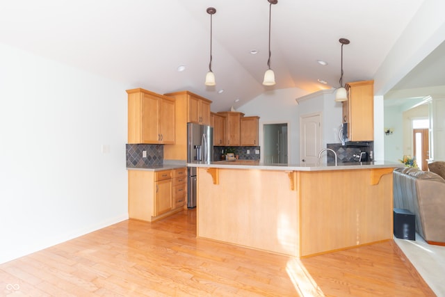 kitchen featuring a kitchen bar, vaulted ceiling, light wood-type flooring, appliances with stainless steel finishes, and kitchen peninsula