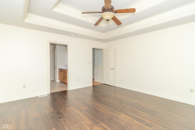 empty room featuring ornamental molding, dark wood-type flooring, ceiling fan, and a tray ceiling