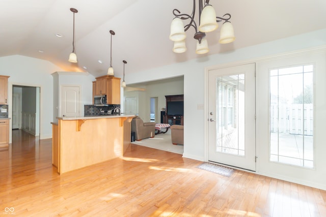 kitchen featuring a kitchen breakfast bar, kitchen peninsula, vaulted ceiling, and decorative light fixtures