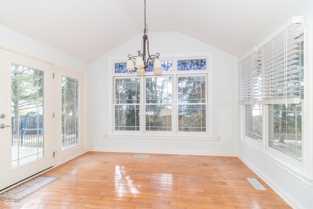 unfurnished dining area featuring lofted ceiling, an inviting chandelier, and light hardwood / wood-style flooring