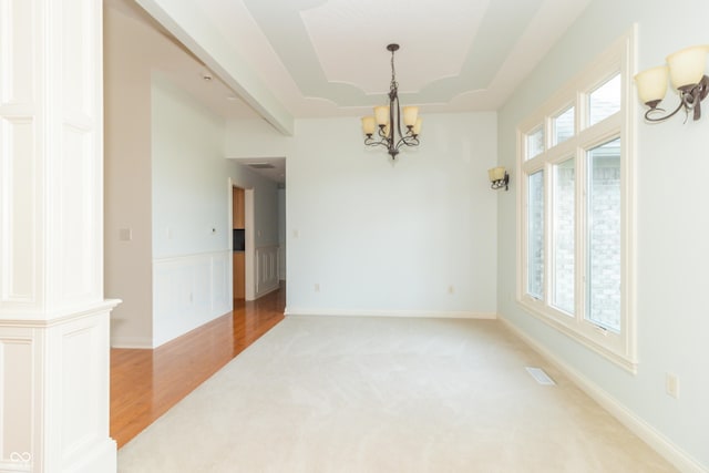 spare room featuring a notable chandelier, light hardwood / wood-style flooring, a raised ceiling, and a healthy amount of sunlight