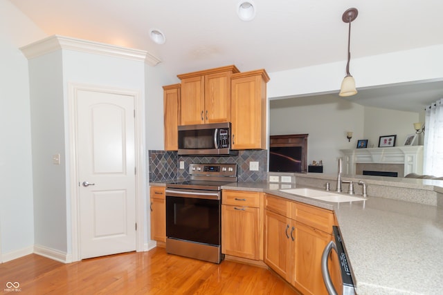 kitchen with appliances with stainless steel finishes, sink, decorative backsplash, hanging light fixtures, and light hardwood / wood-style floors