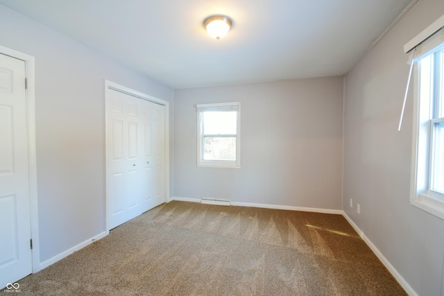 unfurnished bedroom with a baseboard heating unit, carpet floors, and a closet