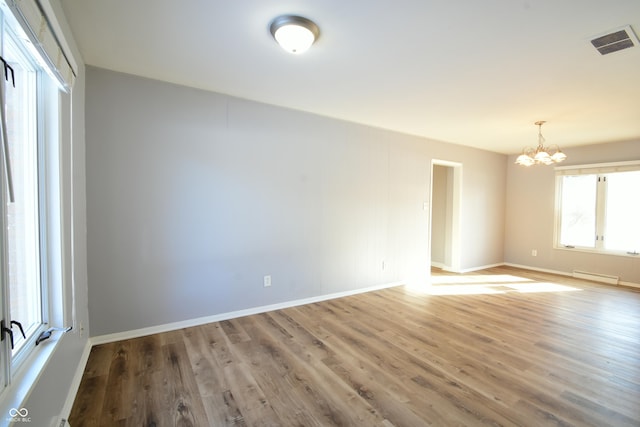 empty room with wood-type flooring, a notable chandelier, and baseboard heating