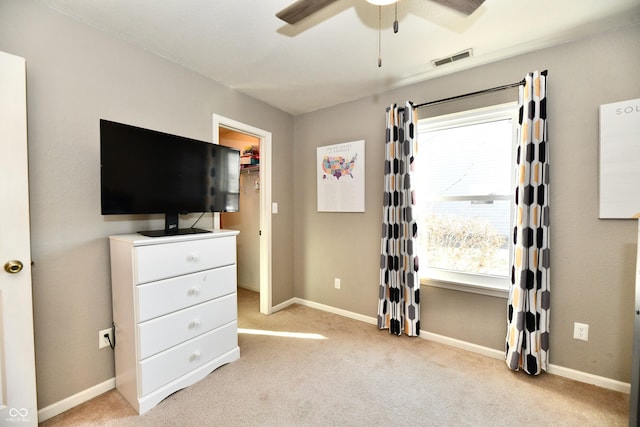 unfurnished bedroom with light carpet, a spacious closet, and ceiling fan