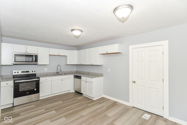 kitchen with stainless steel appliances, sink, white cabinets, and light hardwood / wood-style flooring