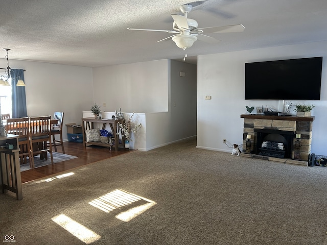 carpeted living room featuring ceiling fan, a stone fireplace, and a textured ceiling