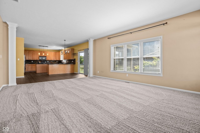 unfurnished living room with dark carpet, decorative columns, and a notable chandelier