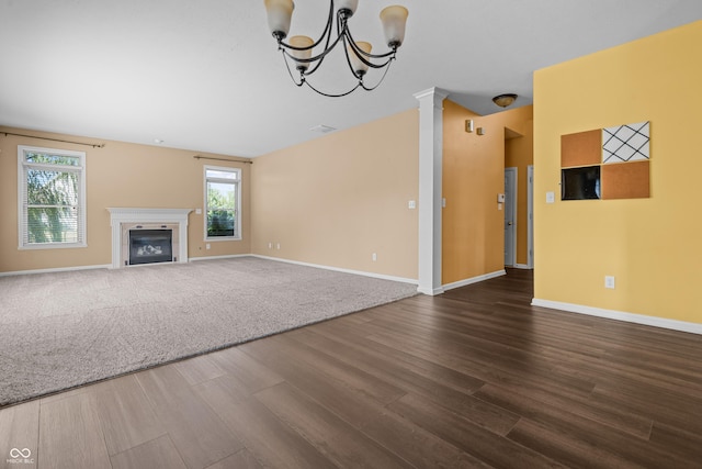 unfurnished living room featuring decorative columns, a healthy amount of sunlight, an inviting chandelier, and dark hardwood / wood-style floors