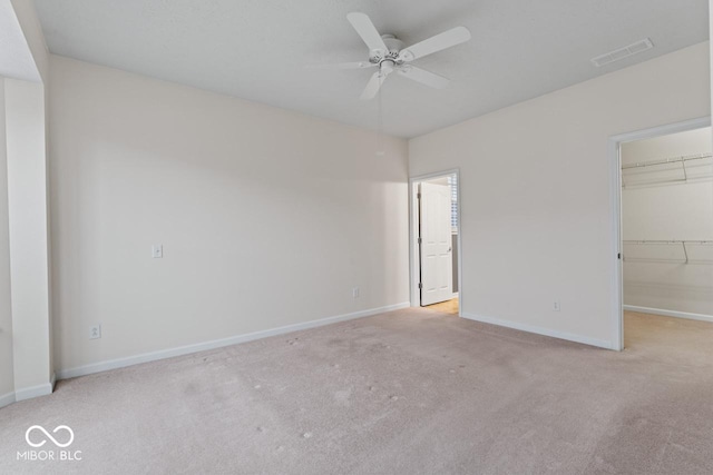 unfurnished bedroom featuring ceiling fan, a walk in closet, a closet, and light carpet