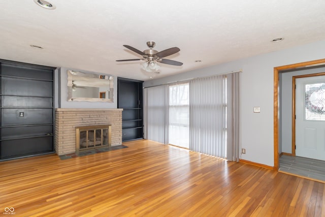 unfurnished living room featuring a brick fireplace, wood-type flooring, and ceiling fan