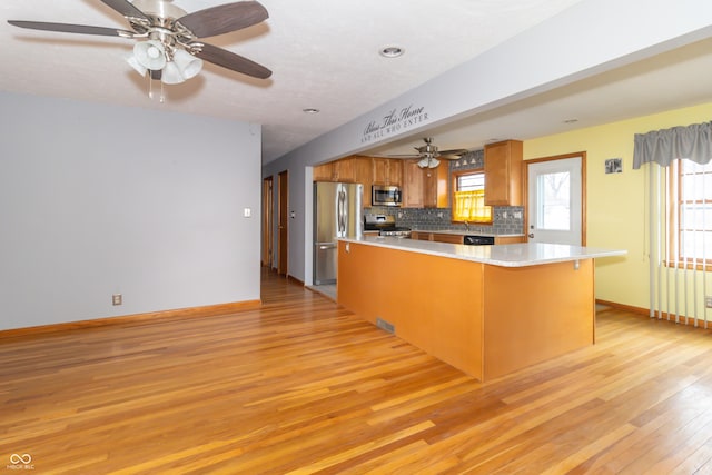 kitchen with tasteful backsplash, appliances with stainless steel finishes, kitchen peninsula, and light hardwood / wood-style flooring