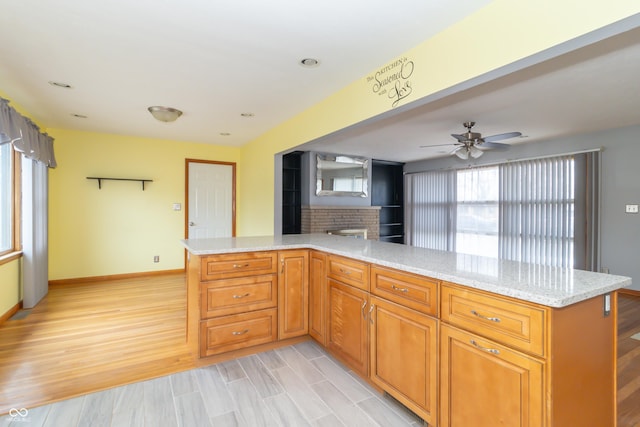 kitchen with decorative backsplash, kitchen peninsula, light stone countertops, and light hardwood / wood-style flooring