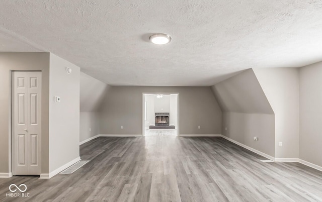 bonus room featuring lofted ceiling, light hardwood / wood-style floors, and a textured ceiling