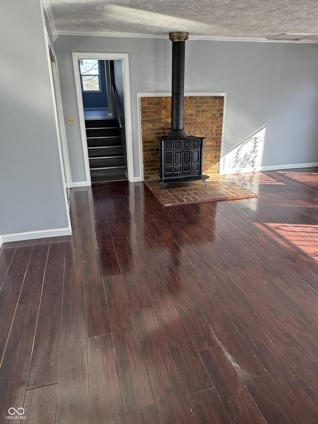 unfurnished living room featuring dark hardwood / wood-style flooring, ornamental molding, a wood stove, and a textured ceiling