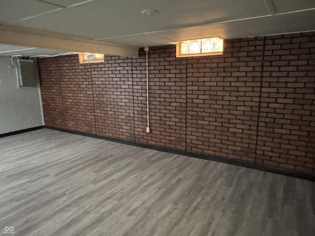 basement featuring brick wall and wood-type flooring