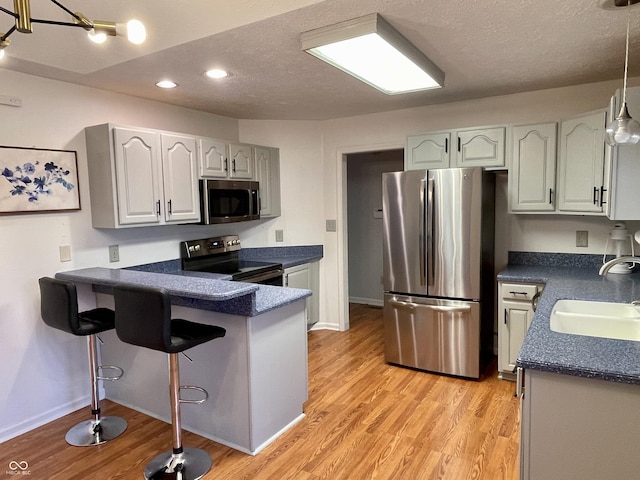 kitchen featuring a breakfast bar, sink, decorative light fixtures, light wood-type flooring, and stainless steel appliances